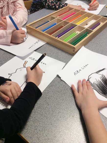 Förskolebarns händer som vilar på ett bord och ritar karaktären Liten.
